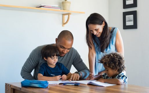 Multiethnic parents helping children with their homework at home. Young father and mother helping sons study at living room. Little boys completing their exercises with the help of dad and mom.