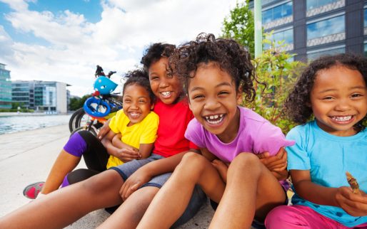 Portrait of four happy African children, age-diverse boys and girls, having fun together outdoors in summertime