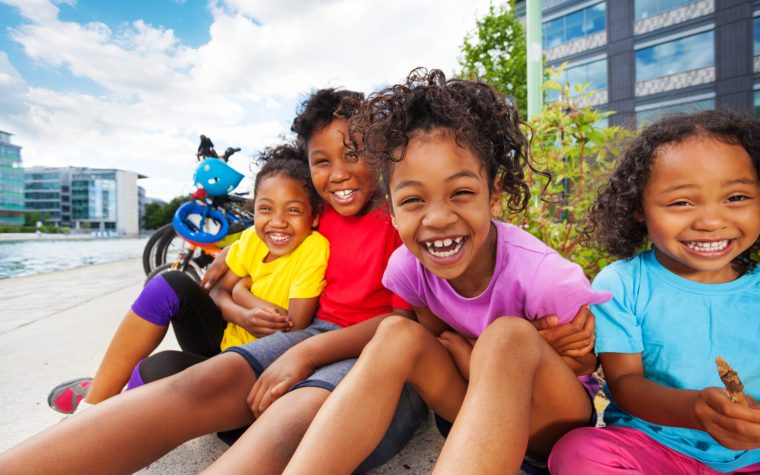 Portrait of four happy African children, age-diverse boys and girls, having fun together outdoors in summertime