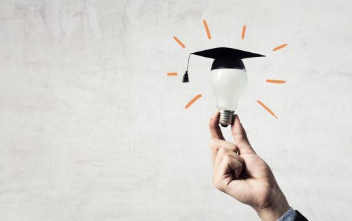 Hand of businessman holding glowing light bulb with graduation hat on it