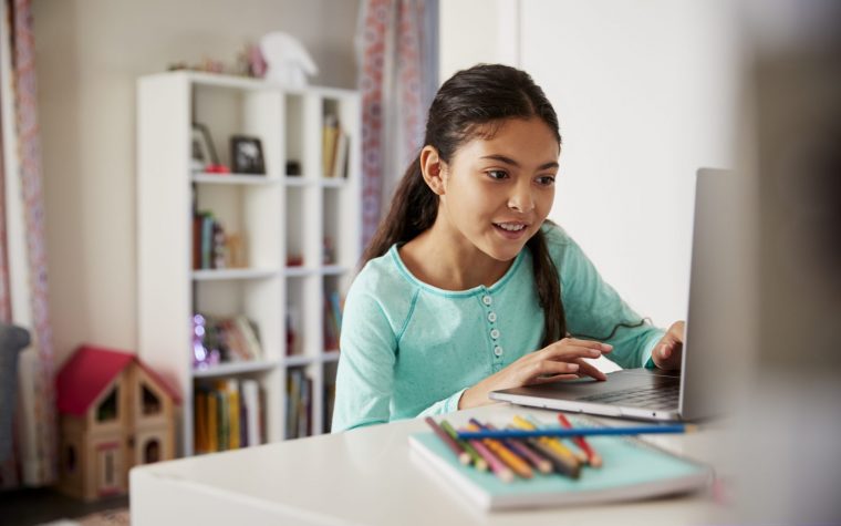 Young Girl Sitting At Desk In Bedroom Using Laptop To Do Homework