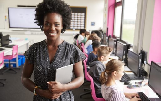 Portrait Of Female Teacher Holding Digital Tablet Teaching Line Of High School Students Sitting By Screens In Computer Class