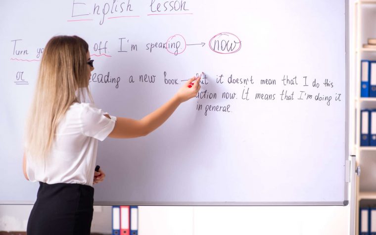 Young female english language teacher standing in front of the blackboard