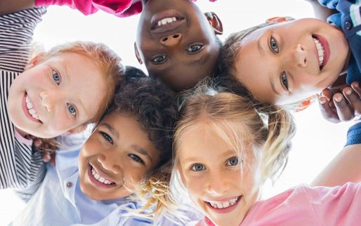 Closeup face of happy multiethnic children embracing each other and smiling at camera. Team of smiling kids embracing together in a circle. Portrait of young boy and pretty girls looking at camera.