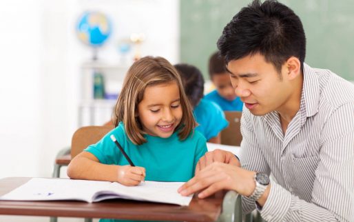 friendly preschool teacher helping little girl with class work