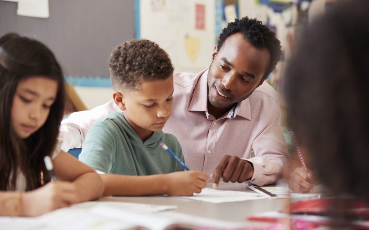 Male teacher working with elementary school boy at his desk