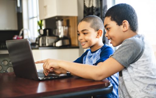 The two Black boy sitting playing on a laptop computer at home