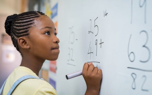 Portrait of african girl writing solution of sums on white board at school. Black schoolgirl solving addition sum on white board with marker pen. School child thinking while doing mathematics problem.