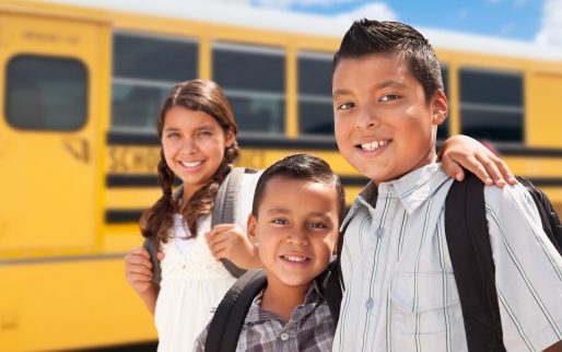 Young Hispanic Boys and Girl Walking Near School Bus.