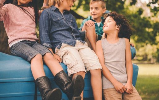 Little asian girl and her friends sitting on an old blue tractor underneath a big leafy tree on the farm having fun playing together