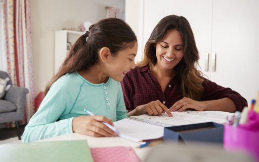 Mother Helping Daughter With Homework Sitting At Desk In Bedroom